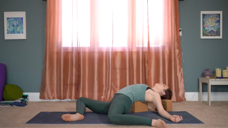 Yoga teaching lying back on blocks placed on a yoga mat during stretches for hips