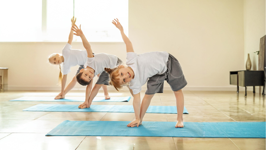 three kids practicing yoga triangle pose with smiles on their faces