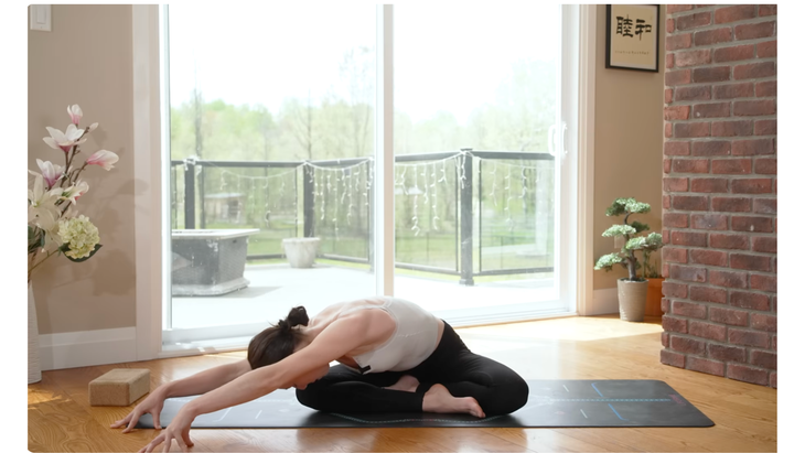 Woman on yoga mat practicing gentle yoga for stress by bending forward while sitting