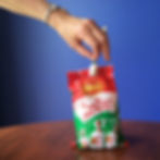 A hand reaching into a packet of Allen's Minties and removing one. Blue wall, wooden table. Pearl ring on her finger, silver watch on her hand.